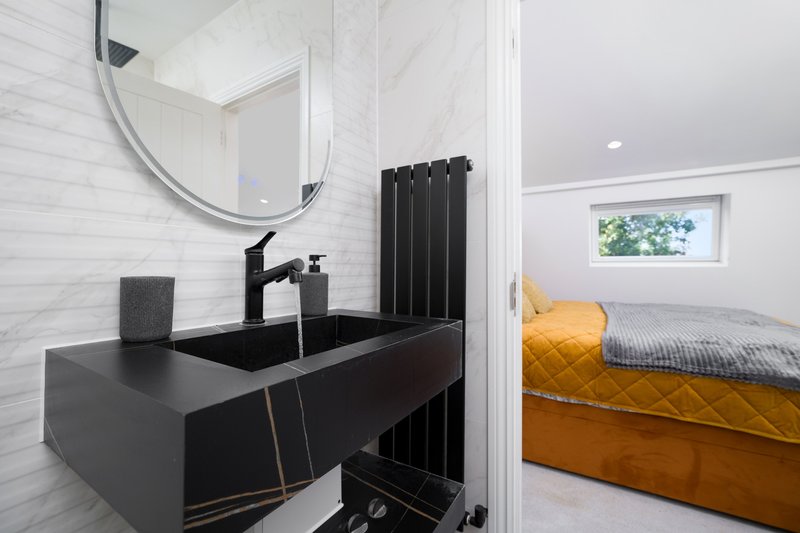 Modern bathroom with black sink, round mirror, white tile walls and view into bedroom