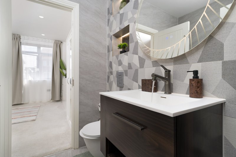Modern bathroom with dark vanity, white sink, geometric tile wall and round mirror