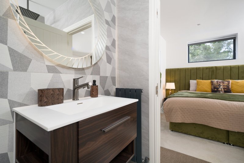 Modern bathroom with dark vanity, white sink, geometric tile wall and bedroom visible through doorway