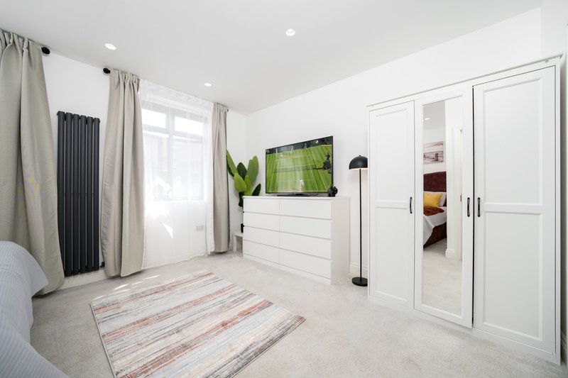 Modern bedroom with white built-in storage, wall-mounted TV, mirrored wardrobe doors and striped rug