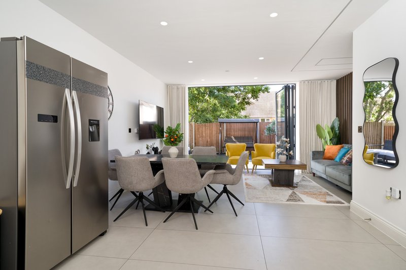 Open-plan kitchen and dining area with stainless steel refrigerator, dining table, and living space beyond