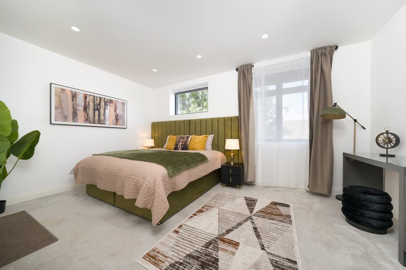 Modern bedroom with olive-green upholstered bed, beige bedding, wooden nightstands, and contemporary furnishings