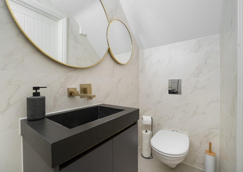 Modern bathroom with marble walls, black vanity sink, brass mirrors and wall-mounted toilet