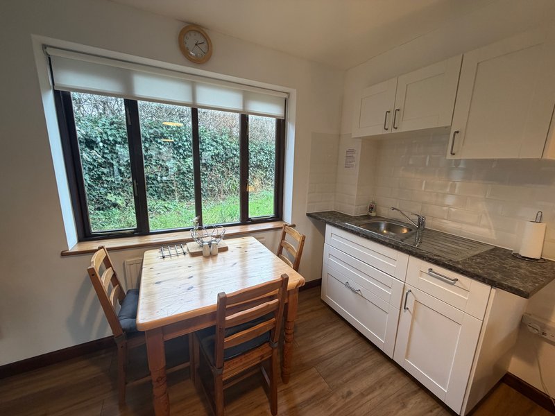 Kitchen with dining table, white cabinetry, dark worktop and large window overlooking garden