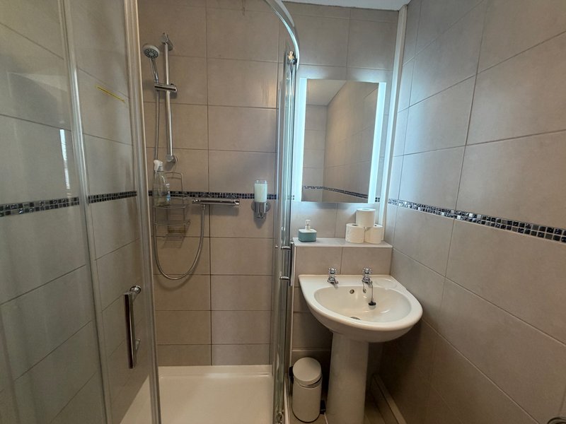 Modern bathroom with shower cubicle, pedestal sink, mirror and tiled walls