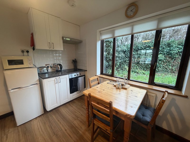 Kitchen-diner with white cabinets, wooden table, chairs and garden view through large windows