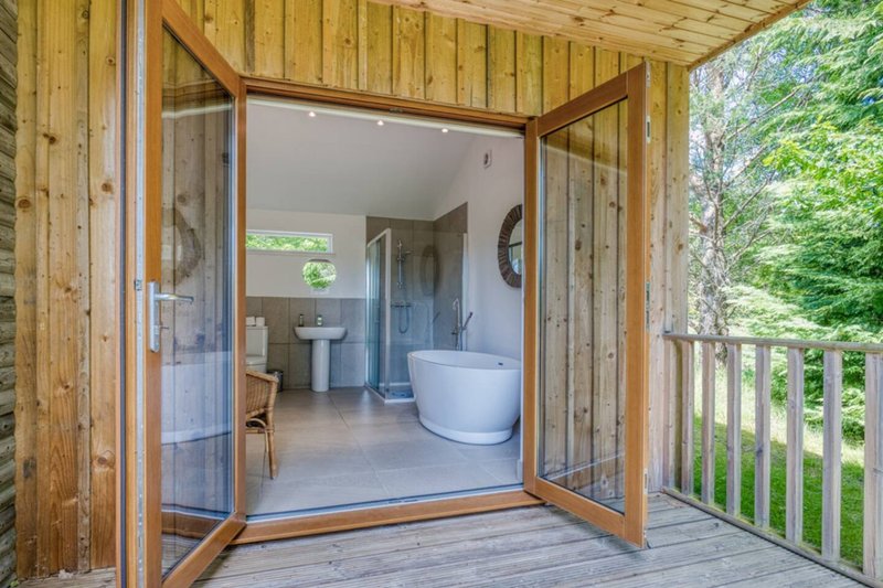 Wooden cabin bathroom with soaking tub, sink, and open glass doors to deck