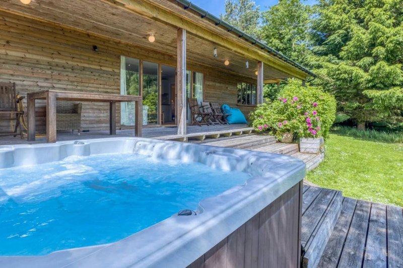 Wooden lodge with hot tub, deck, chairs and garden surroundings