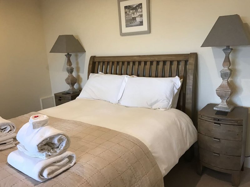 Bedroom with double bed, wooden headboard, white pillows, beige bedding, two bedside lamps and tables