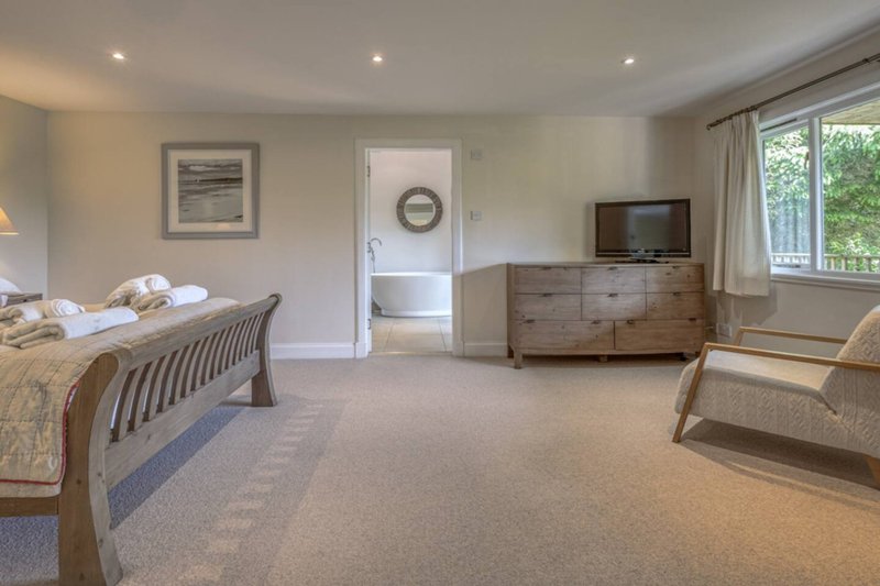 Spacious bedroom with wooden bed frame, dresser, armchair, and ensuite bathroom visible