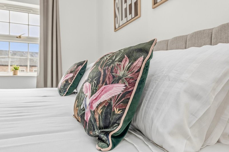 Bright bedroom with double bed, decorative floral pillows, white bedding and window view