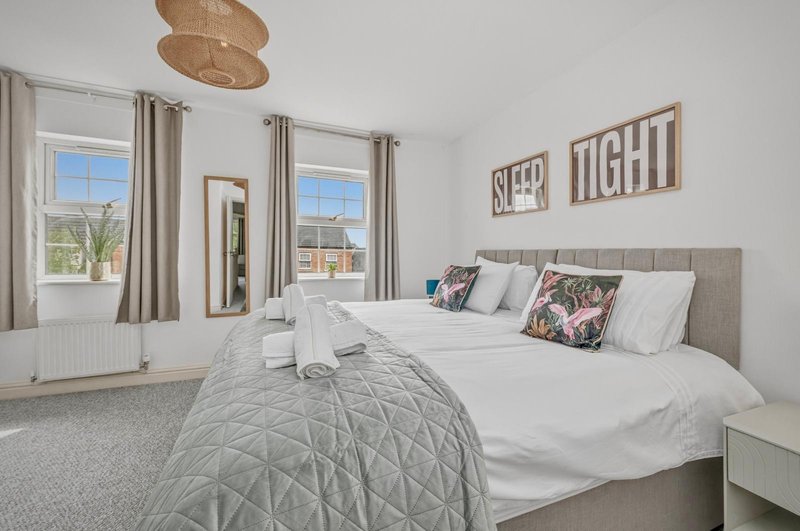 Bright modern bedroom with double bed, grey headboard, patterned cushions and wall decor