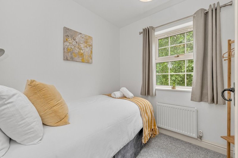 Bright bedroom with single bed, yellow cushions, window with garden view, wooden ladder shelf
