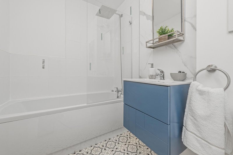 Modern bathroom with blue vanity, white subway tiles, glass shower enclosure and potted plant