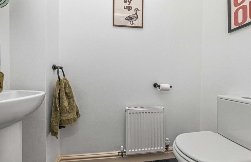Small bathroom with toilet, sink, radiator and towel rack on white walls