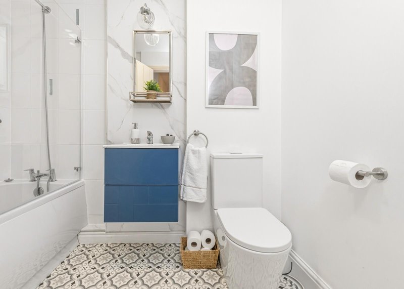 Modern bathroom with blue vanity, white toilet, shower enclosure and patterned floor tiles