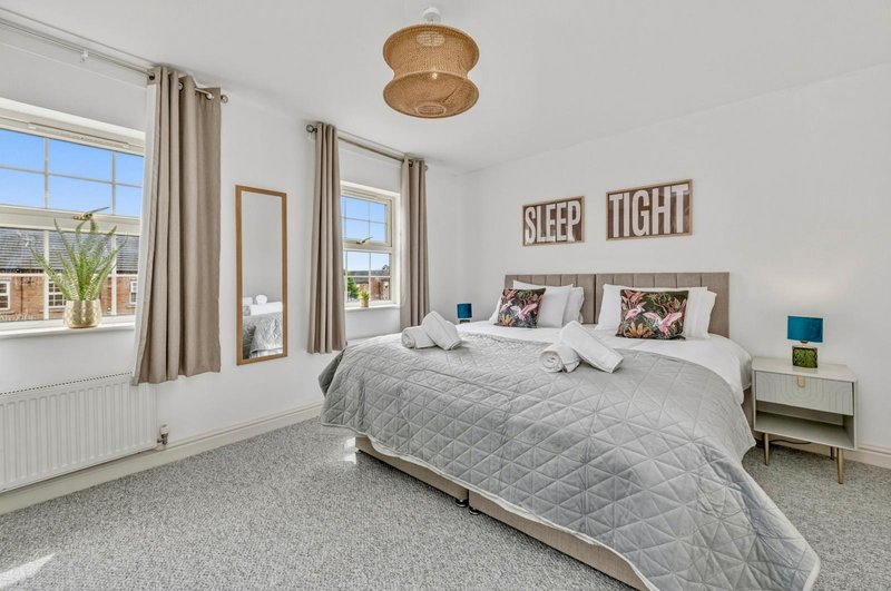 Bright bedroom with double bed, grey quilted bedding, wooden ceiling light, and large windows