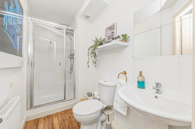 Modern bathroom with shower enclosure, white sink, toilet, wooden floor and shelving