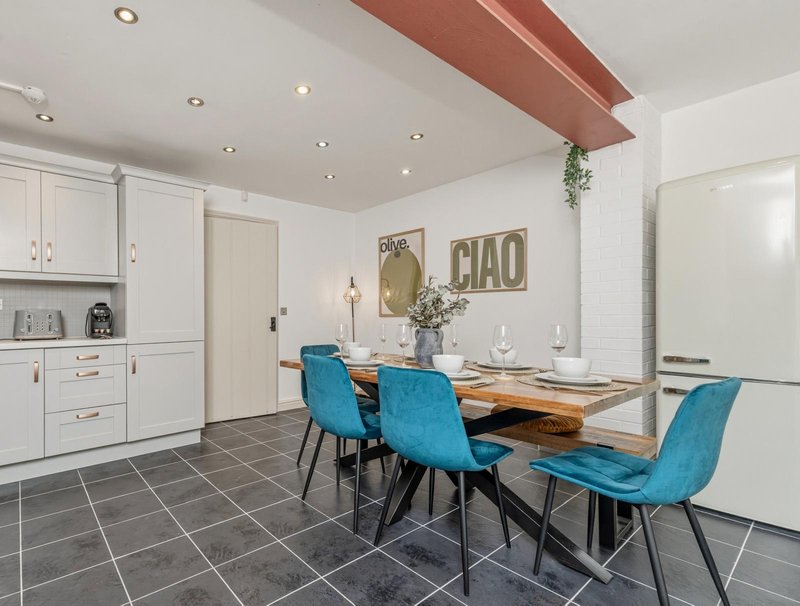 Modern kitchen-diner with white cabinetry, wooden dining table, turquoise chairs and decorative wall art