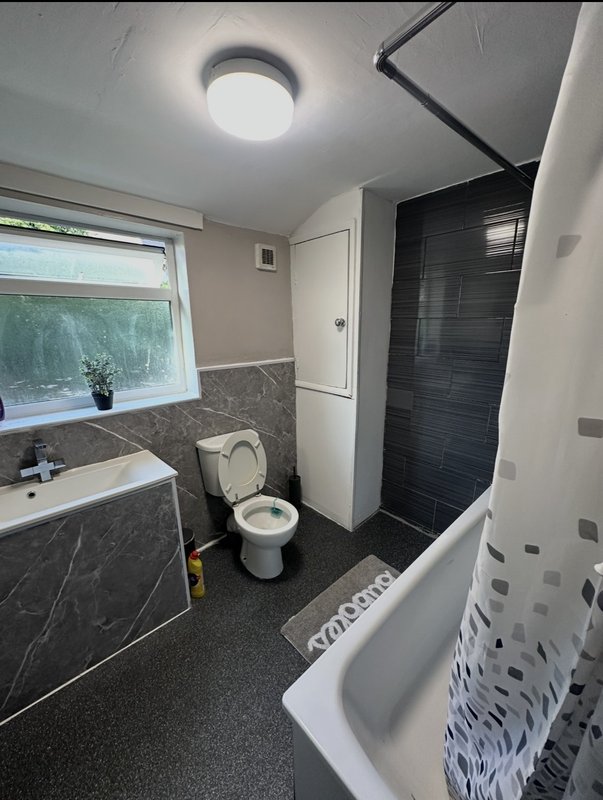 Modern bathroom with dark tile walls, white toilet, sink, shower enclosure and window