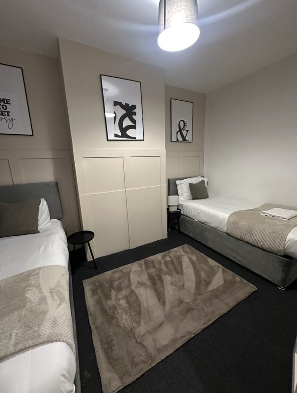 Twin bedroom with two single beds, cream wardrobe, framed wall art, and dark flooring.