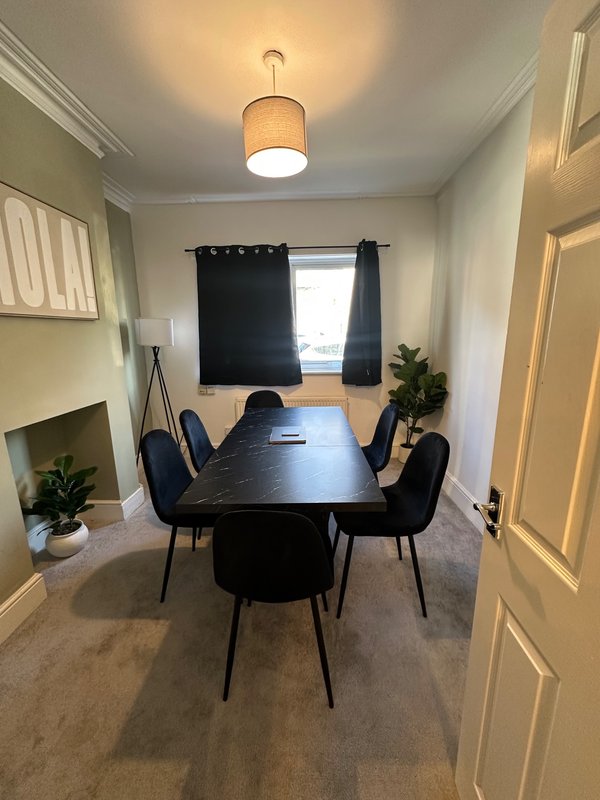 Dining room with black table, four chairs, pendant light and window with dark curtains