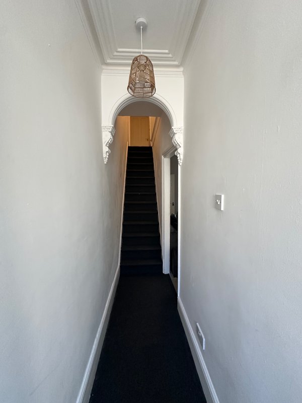 Long narrow hallway with black runner carpet, white walls, and staircase visible at far end