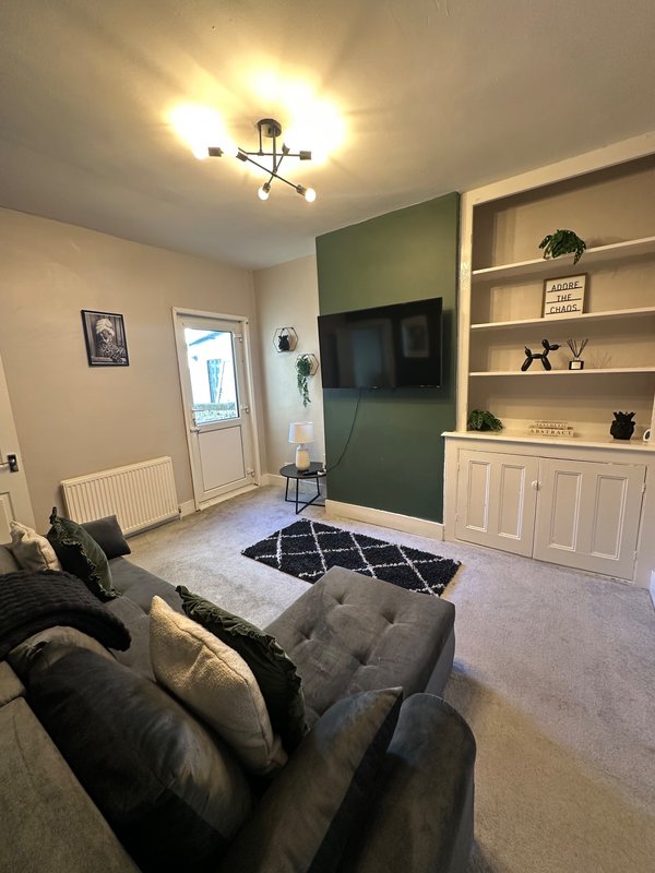 Living room with gray sofa, TV mounted on green accent wall, built-in shelving, and ceiling light fixture