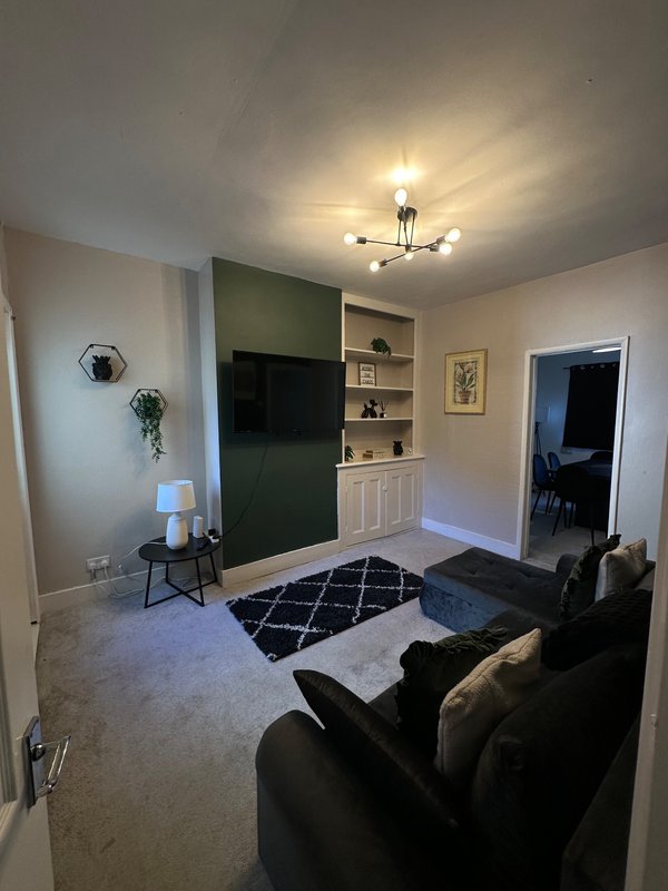 Modern living room with black sofa, wall-mounted TV, built-in shelving, and geometric area rug