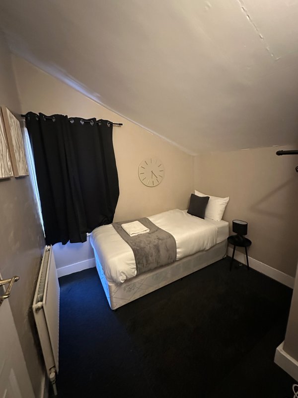 Bedroom with double bed, black curtains, wall clock, and blue carpet flooring
