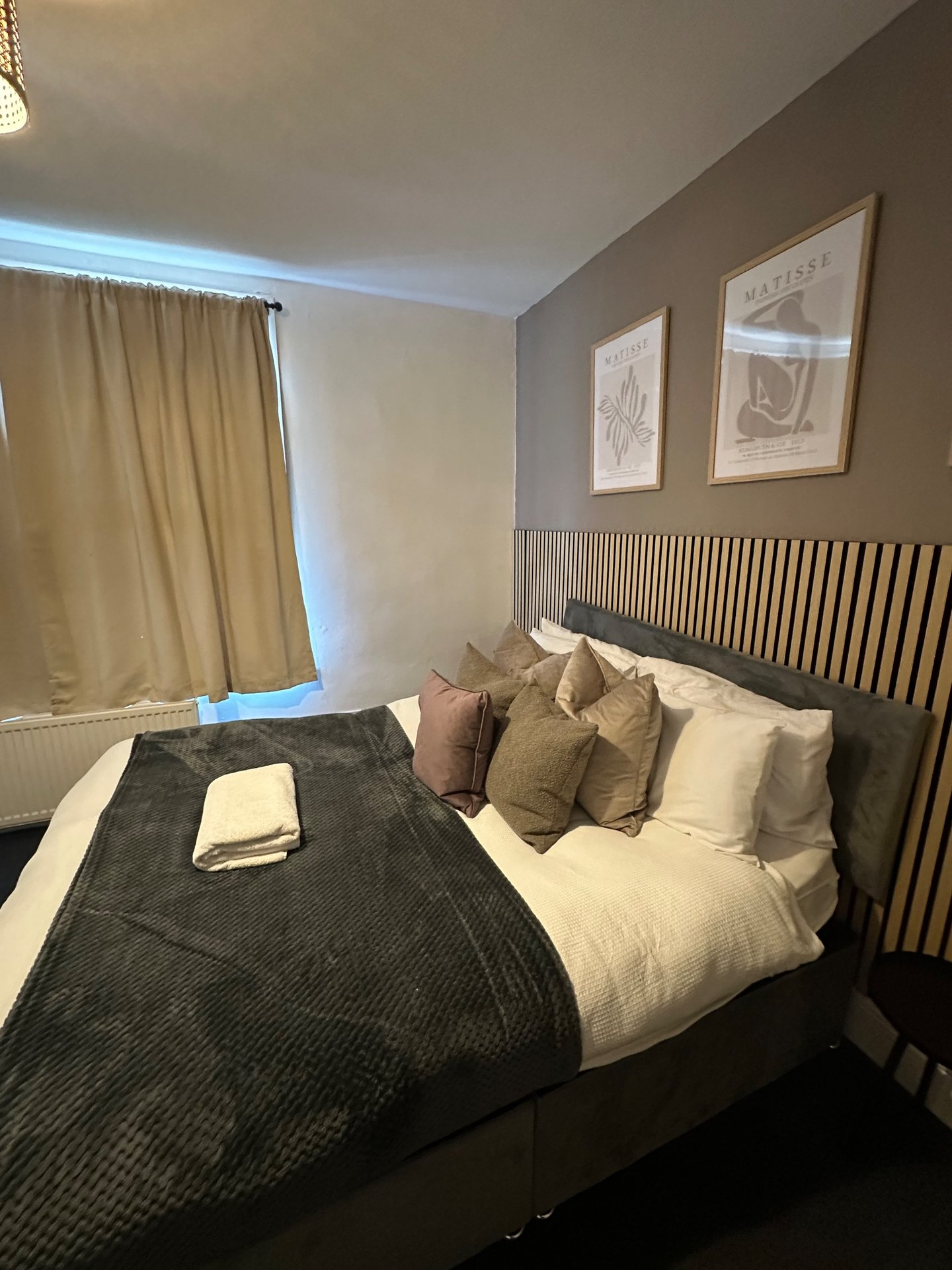 Modern bedroom with double bed, neutral bedding, decorative pillows, radiator and framed wall art