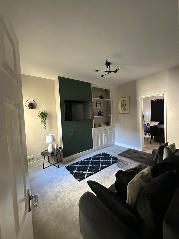 Modern living room with black sofa, dark TV wall unit, geometric rug and wall-mounted lighting