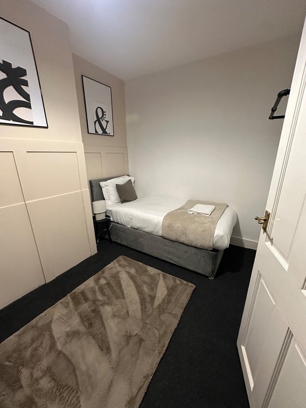 Compact bedroom with single bed, black flooring, white wardrobes and framed wall art
