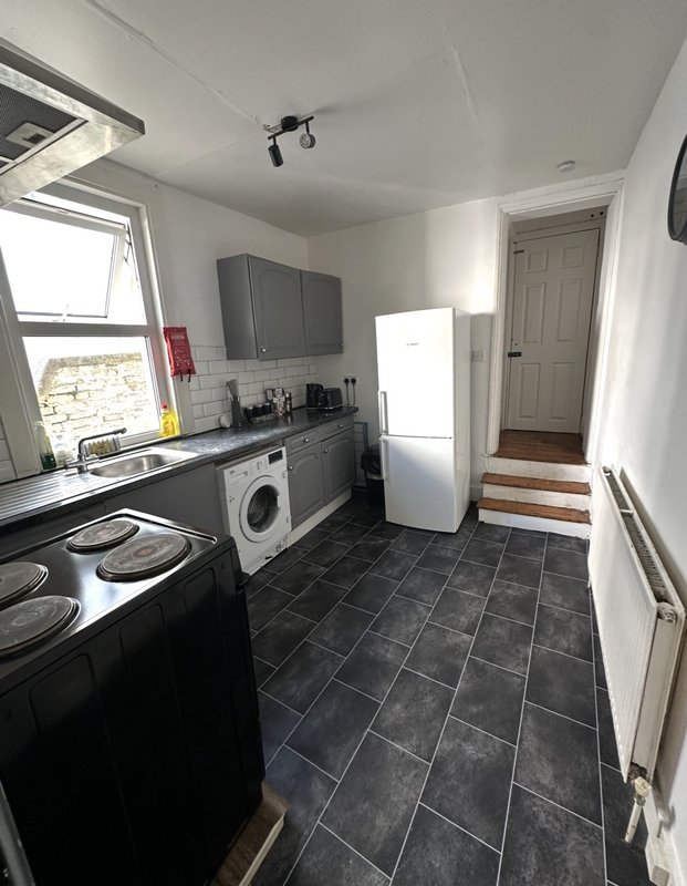 Modern kitchen with black appliances, white fridge, washing machine, and dark tile flooring