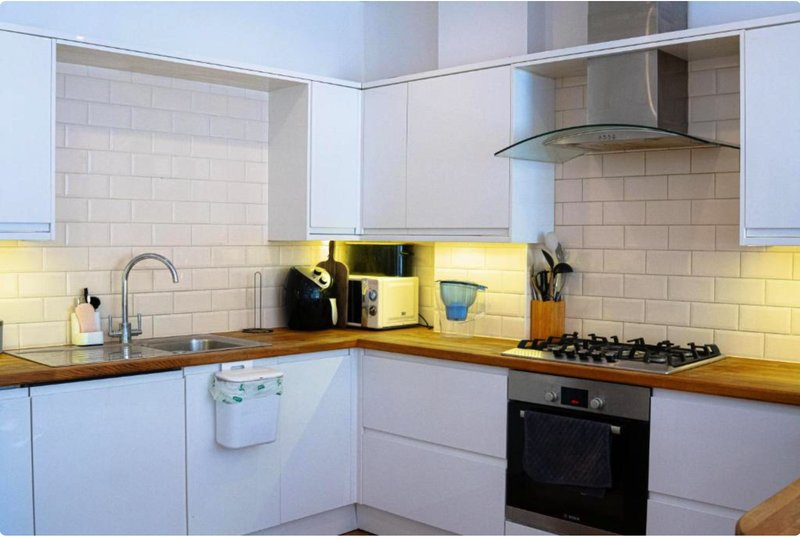 Modern kitchen with white cabinets, yellow backlighting, gas hob and stainless steel extractor hood