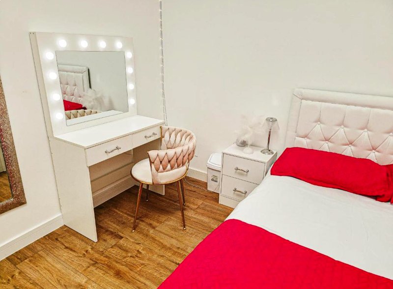 Bright bedroom with vanity mirror, makeup chair, double bed with red bedding and white headboard
