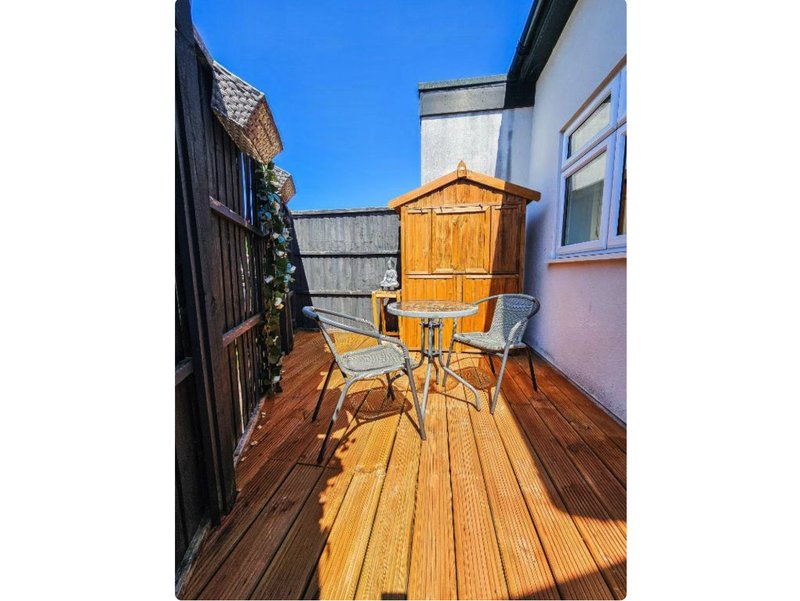 Narrow wooden deck with two chairs, yellow shed, and surrounding fencing