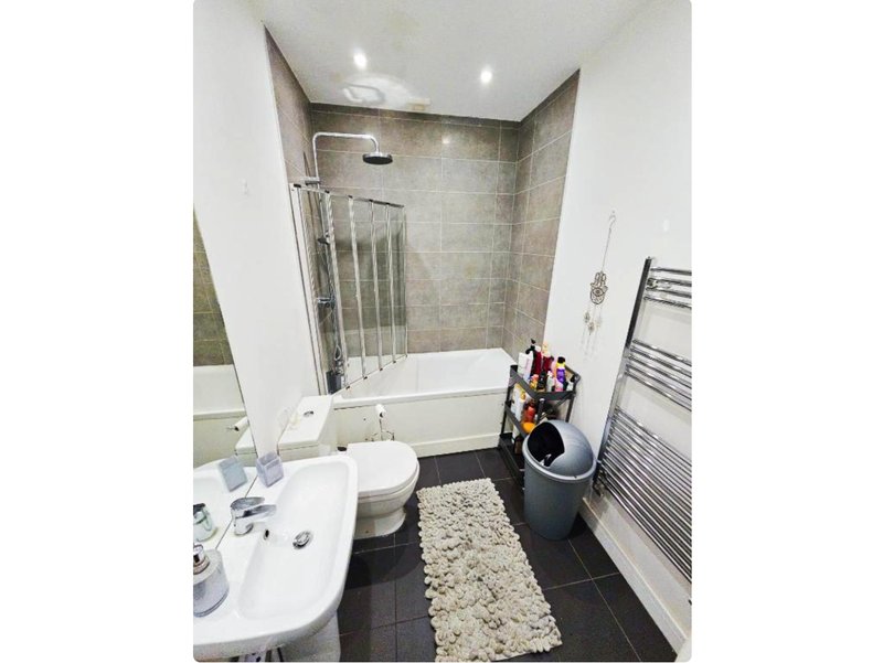 Modern bathroom with white sink, toilet, bath with glass screen and heated towel rail