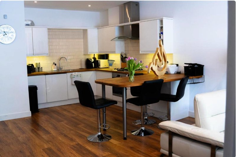 Modern kitchen and dining area with yellow accents, wooden table, black chairs and white cabinetry