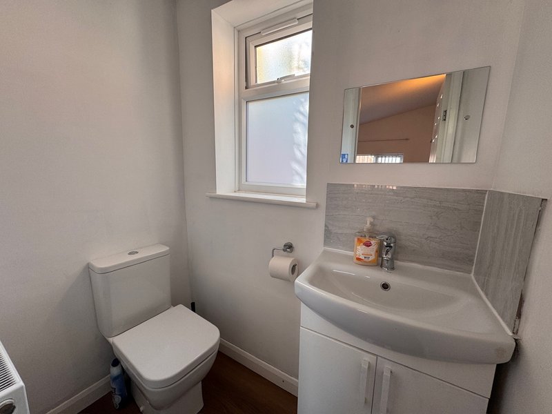 Small bathroom with toilet, corner sink, mirror, and window with natural light