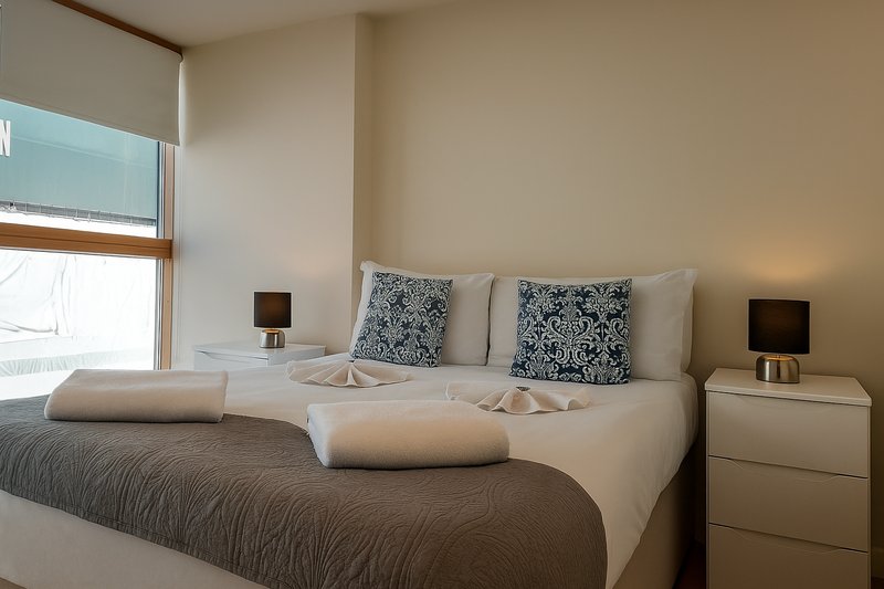 Modern bedroom with double bed, patterned cushions, bedside tables with lamps and window.