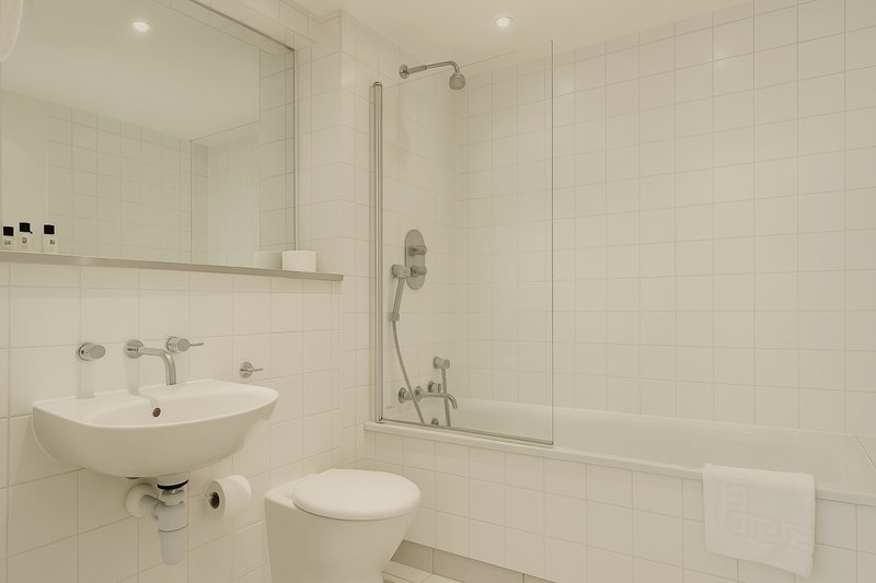 Modern bathroom with white tiles, curved basin sink, toilet, and glass-enclosed shower area