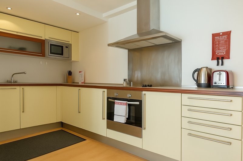 Modern kitchen with yellow cabinets, stainless steel appliances, and wooden worktops