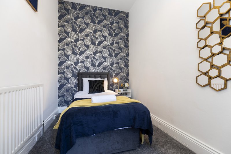 Small bedroom with single bed, navy bedding, patterned headboard and gold wall decor