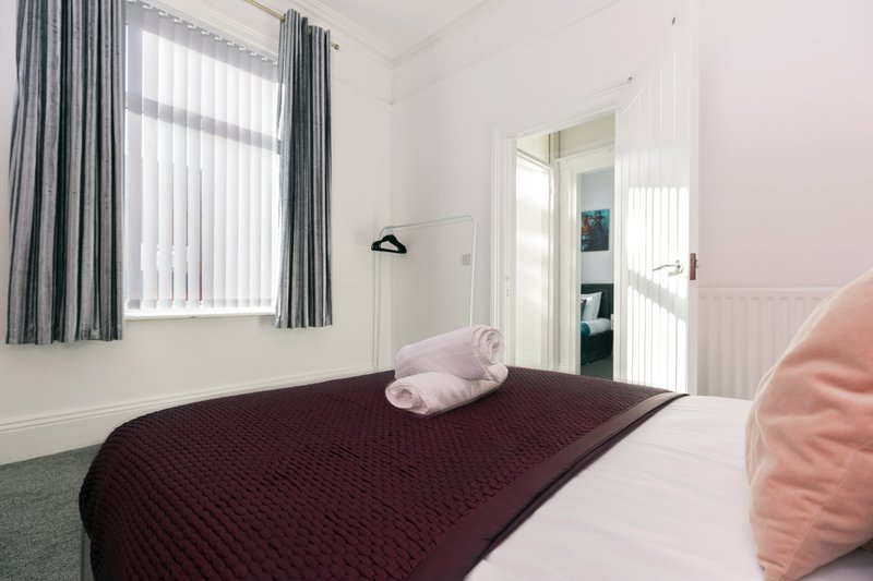 Bright bedroom with double bed, burgundy bedding, pink pillows, and large window with grey curtains