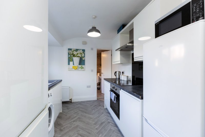 Modern galley kitchen with white cabinetry, black appliances, herringbone flooring and pendant lighting