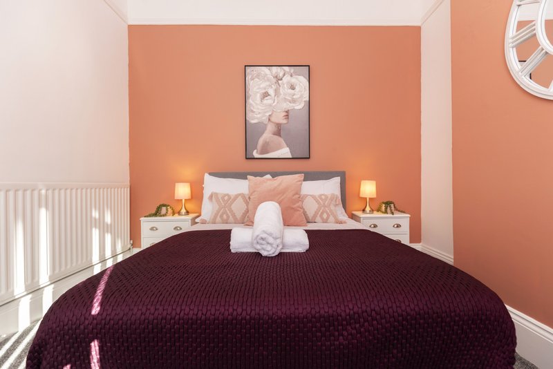Bedroom with double bed, burgundy bedspread, peach-colored walls and framed artwork above headboard