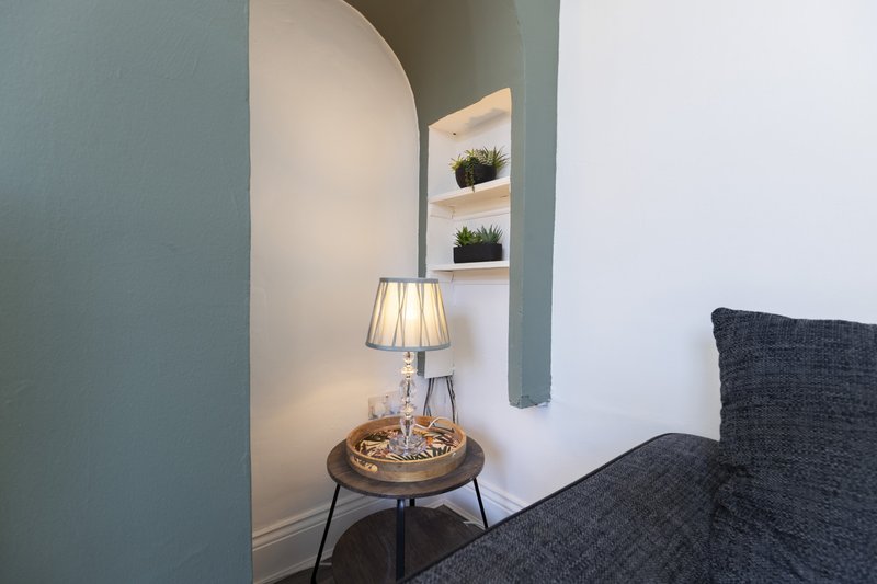 Bedroom corner with table lamp, small potted plants on shelf, and gray upholstered furniture