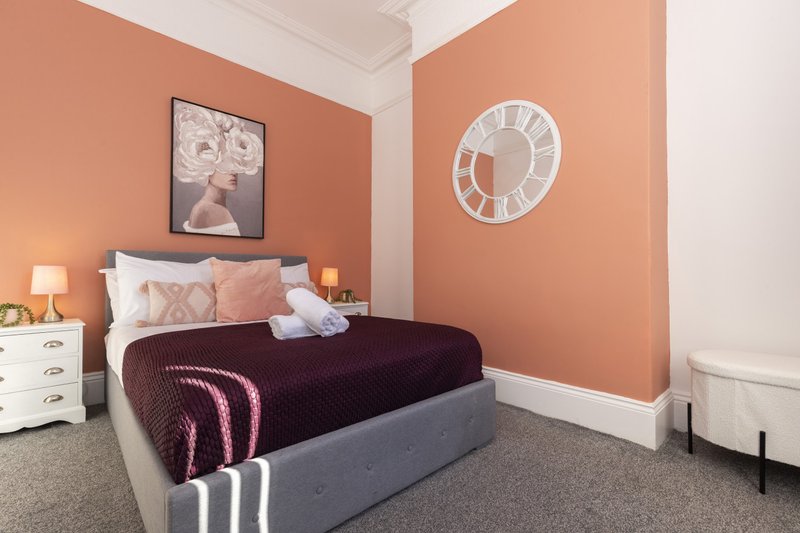 Bedroom with double bed, coral walls, white clock, framed art and bedside lamp