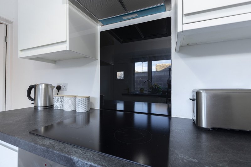 Modern kitchen with dark countertop, stainless steel appliances, white cabinets and black glass doors